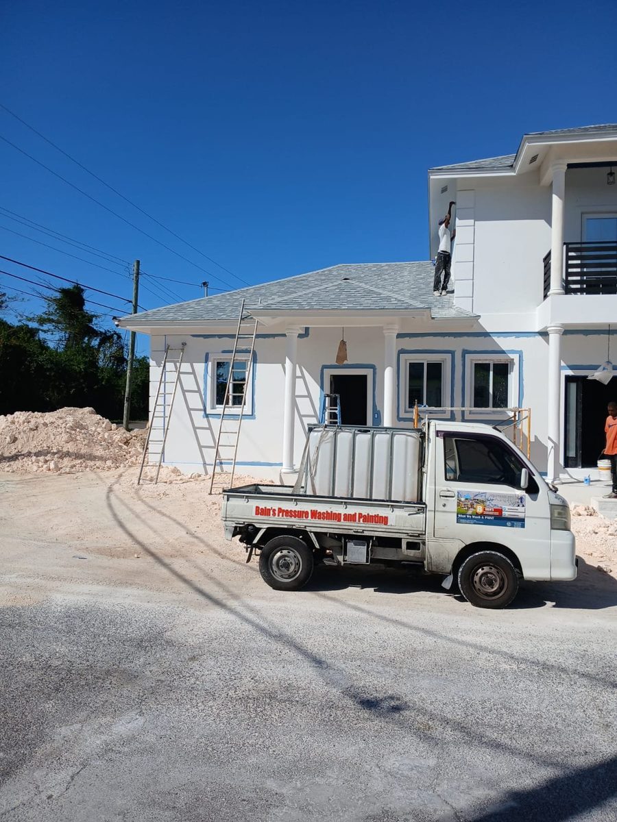 White and blue home being painted with company truck on site